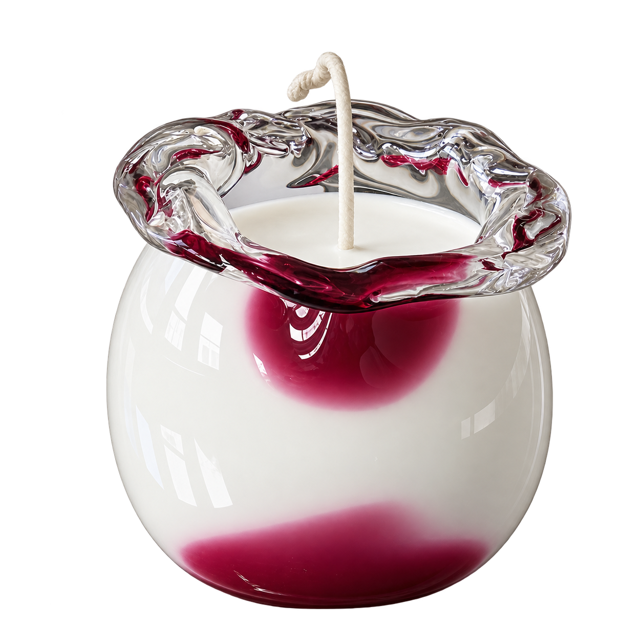 Candle in a sculptural clear glass vessel with deep red accents and a knotted wick.